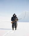 AZ ESZKIMÓ FÉRFI. Mike (az eszkimók napjainkban nyugati nevet viselnek) fókavadászként dolgozik egy távoli, apró grönlandi faluban, a sarkkörtől északra. A sörétes puskáját a jegesmedvék elleni védelem miatt hordja magánál, akik szabadon kóborolnak ezen a jégbe fagyott vidéken. A képen éppen pihenőt tart egy kutyaszánon megtett hosszú út közben. A világnak több ilyen varázslatos vidékre lenne szüksége.